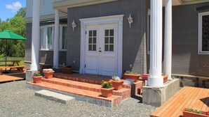 Un edificio de dos plantas con puerta frontal blanca, columnas y un patio cubierto con mesas y sillas al aire libre.