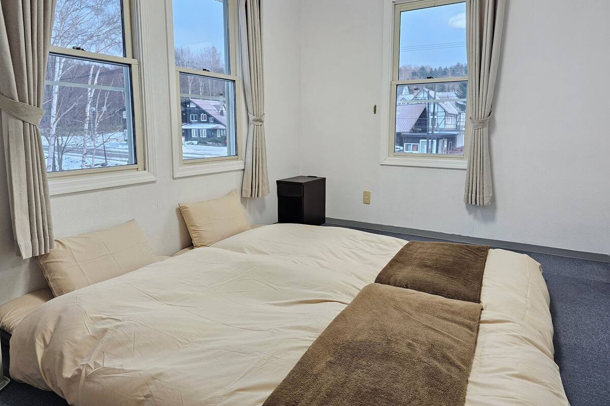 A bedroom with a bed, two windows, and a nightstand.