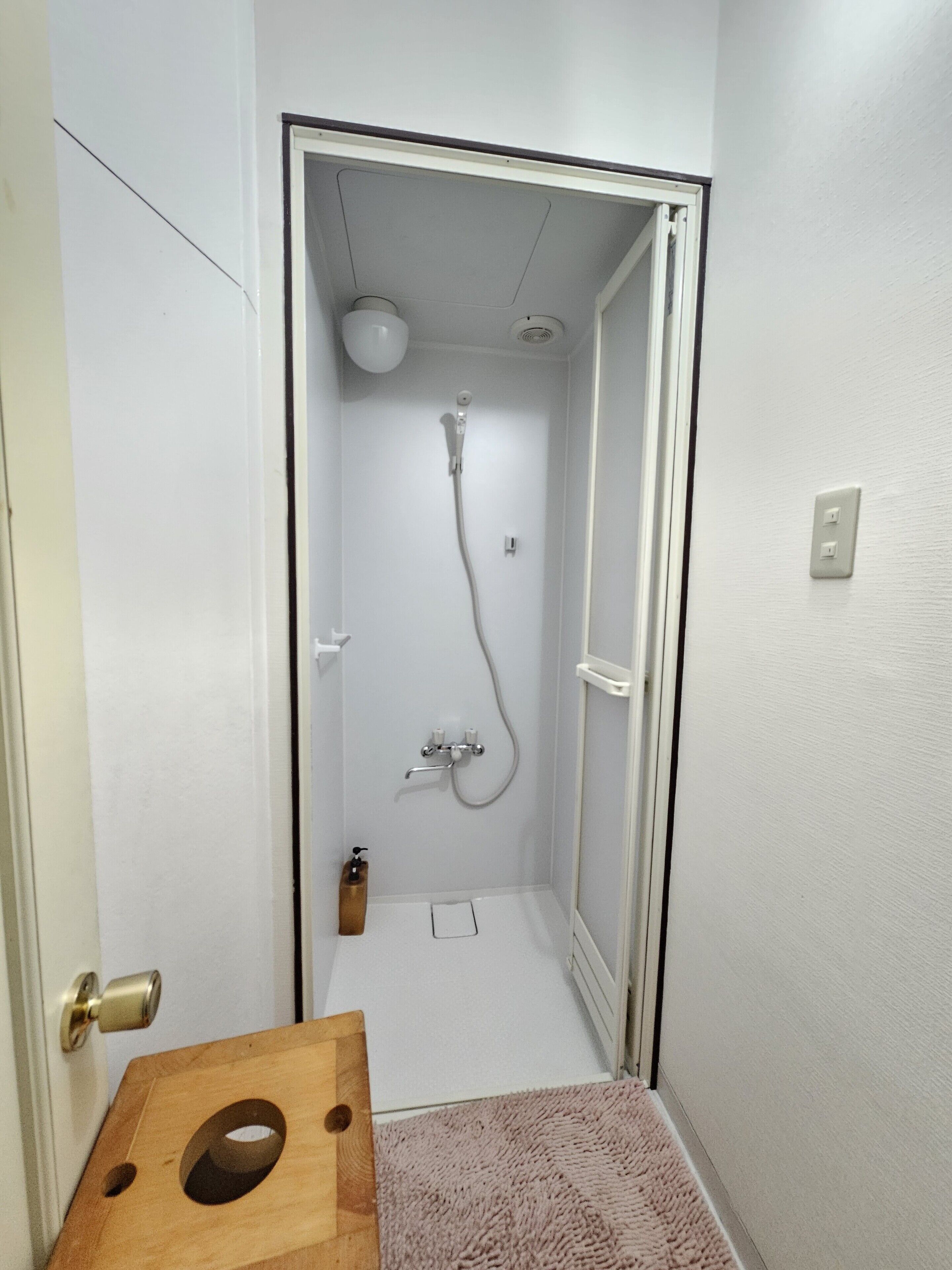 Un baño pequeño y estrecho con ducha, inodoro y un taburete de madera.