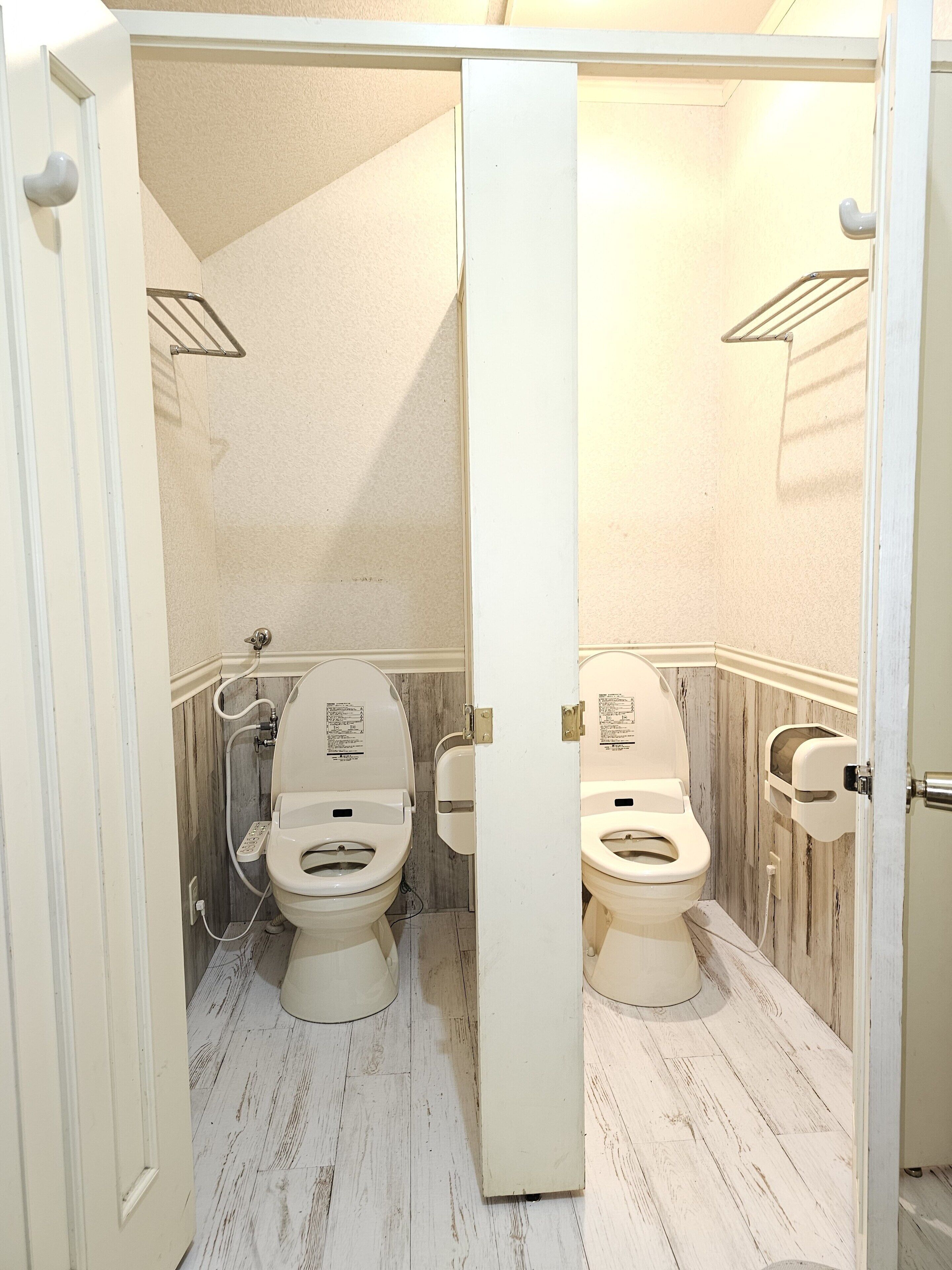 Un baño pequeño y estrecho con dos inodoros, paneles de madera y una puerta blanca.