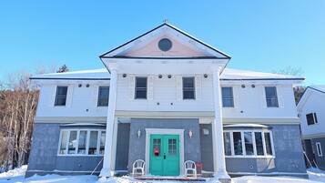 A two-story house with a green front door, white shutters, and a grey facade.