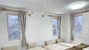 Habitación con cuatro camas dispuestas en forma de U, ventanas amplias con cortinas y una lámpara en el techo.