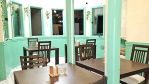 Un comedor con mesas y sillas de madera, paredes pintadas de verde y ventanas con cortinas.