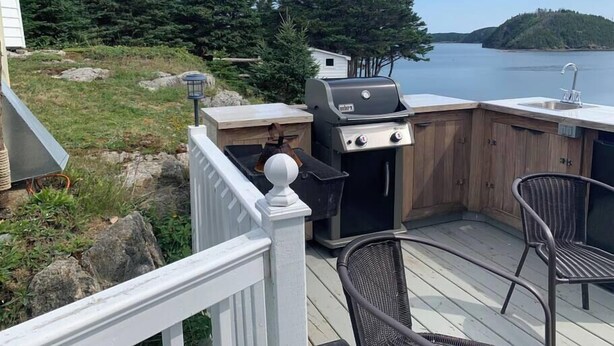 An outdoor deck with a grill, a sink, and a chair.
