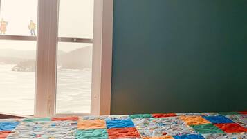 Enjoy a serene view of the water from this cozy room, featuring a colorful quilted bedspread and a large window.