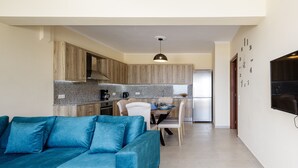 A modern kitchen with wooden cabinets, a dining area with a table and chairs, and a living room with a blue sofa. - Karma House (Rethimno)