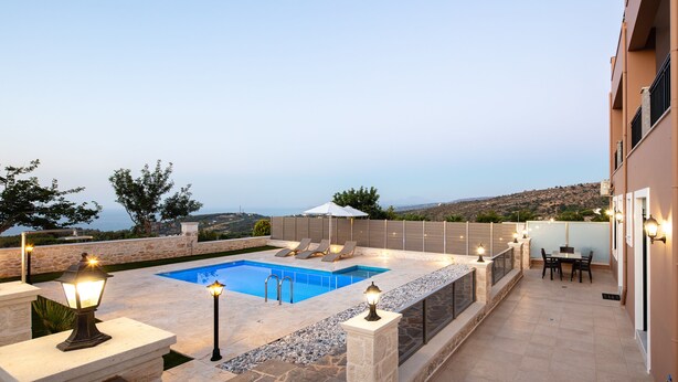 A rooftop pool area with a view of the sea, stone walls, and outdoor furniture. - Karma House (Rethimno)