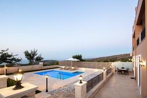 A rooftop pool area with a view of the sea, stone walls, and outdoor furniture. - Karma House (Rethimno)