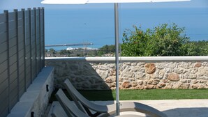 A poolside area with a stone wall and a view of the sea. - Karma House (Rethimno)