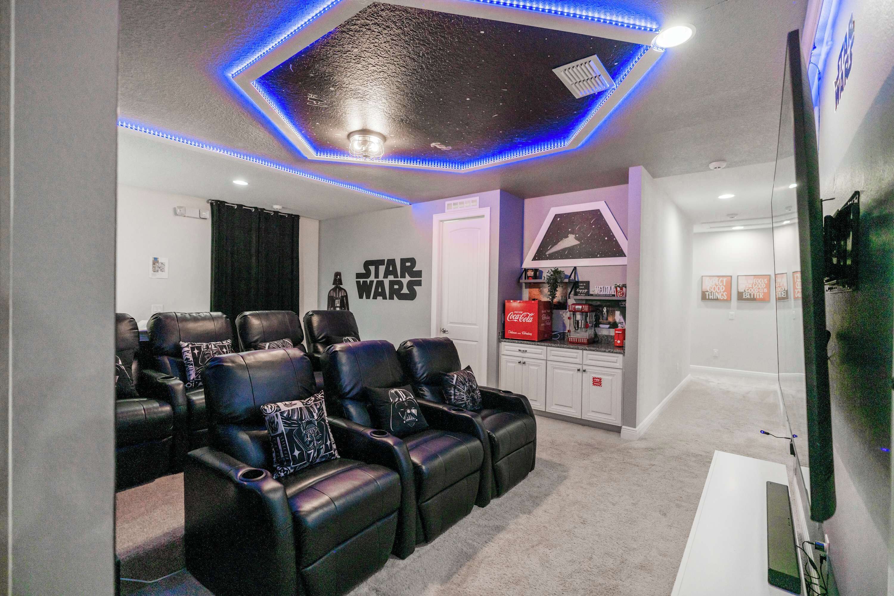 Une salle de cinéma maison équipée de fauteuils inclinables en cuir, d’un décor mural sur le thème de Star Wars et d’un plafond doté de lumières LED bleues.