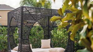 Un espace extérieur aménagé avec des meubles en osier noir et des coussins, entouré d’une terrasse en briques et de verdure.