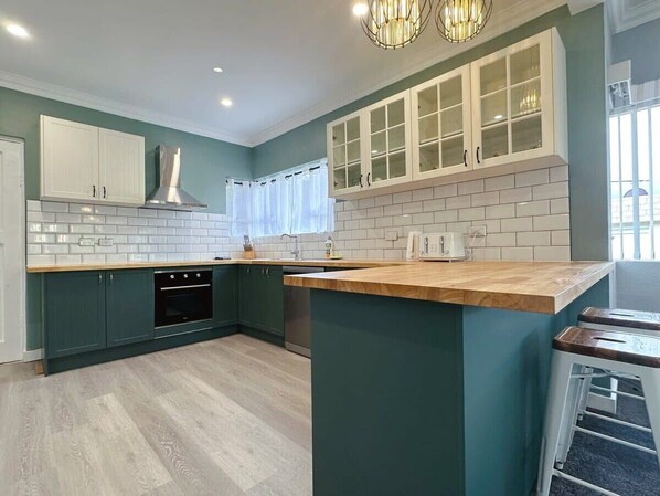 A modern kitchen with teal cabinetry, white countertops, and a central island. - SandyBay Garden Hideaway (Sandy Bay)