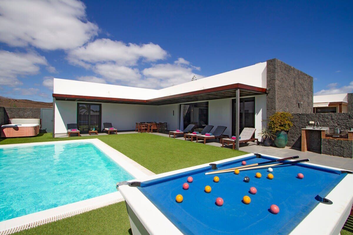 Un espace piscine extérieur moderne, doté d’une table de billard et de chaises longues.