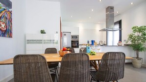 A modern kitchen with white cabinets, a stainless steel range hood, and a dining area with wicker chairs and a wooden table. - Villa Zanata with air conditioning and hot tub (Puerto del Carmen)