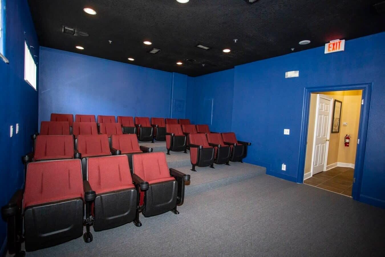 A cinema room with rows of red and black seats, blue walls, and an exit sign.