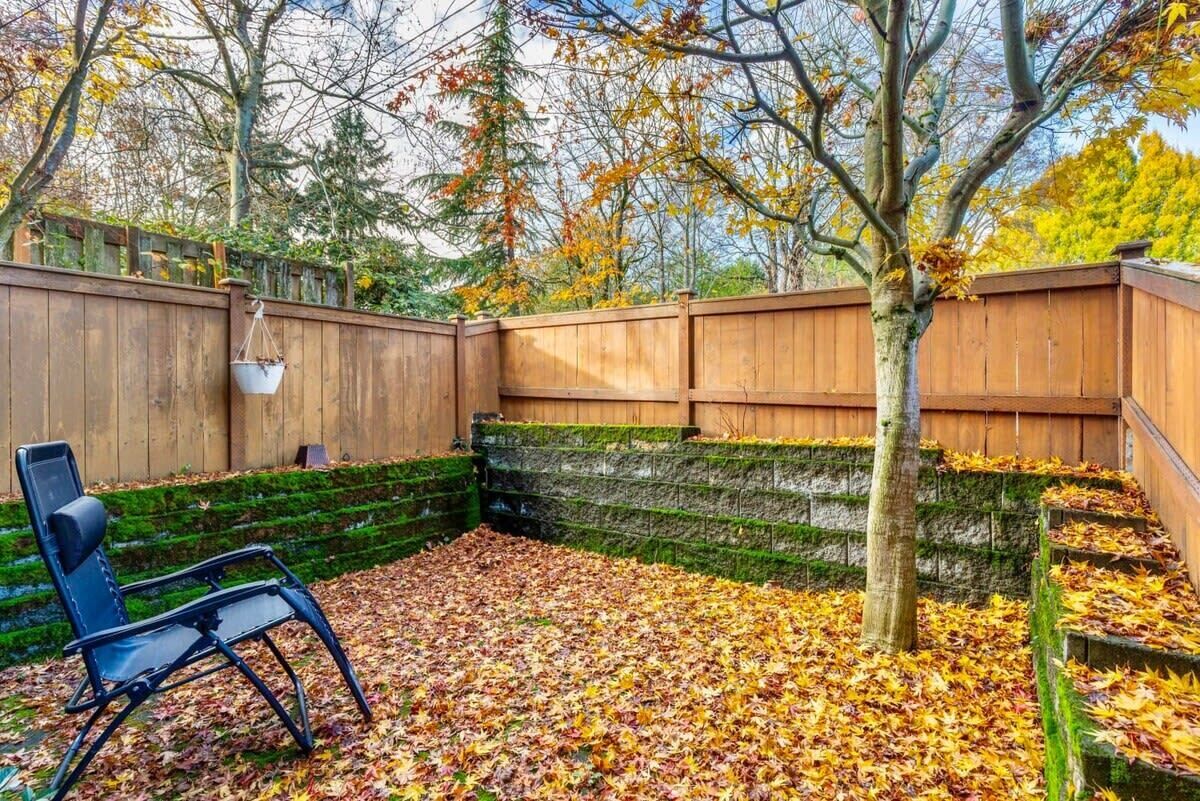 Une terrasse en bois avec une chaise en métal, entourée d’une clôture en bois et d’un arbre.