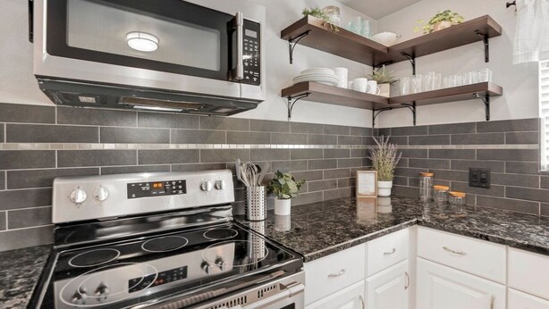 A modern kitchen with a stainless steel microwave, double oven, and granite countertop. There are white cabinets and a backsplash of dark tiles. - Lil' Love Shack ~ Private Yard (Loveland)
