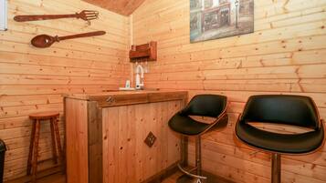 Een houten interieur met een bar, twee zwarte barkrukken, een houten kruk en een houten wand met een afbeelding.