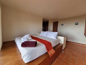 Habitación de hotel con una cama grande, una mesita de noche, una manta roja y una toalla blanca sobre la cama.