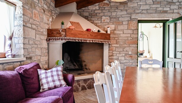 Una sala de estar acogedora con una chimenea de piedra, un sofá morado y una mesa de comedor de madera.