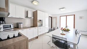 A modern kitchen with white cabinets, a microwave, a coffee maker, and a dining area with a glass table and chairs.