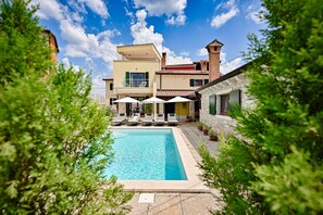 A swimming pool with lounge chairs and umbrellas, surrounded by buildings with balconies and a clear blue sky.