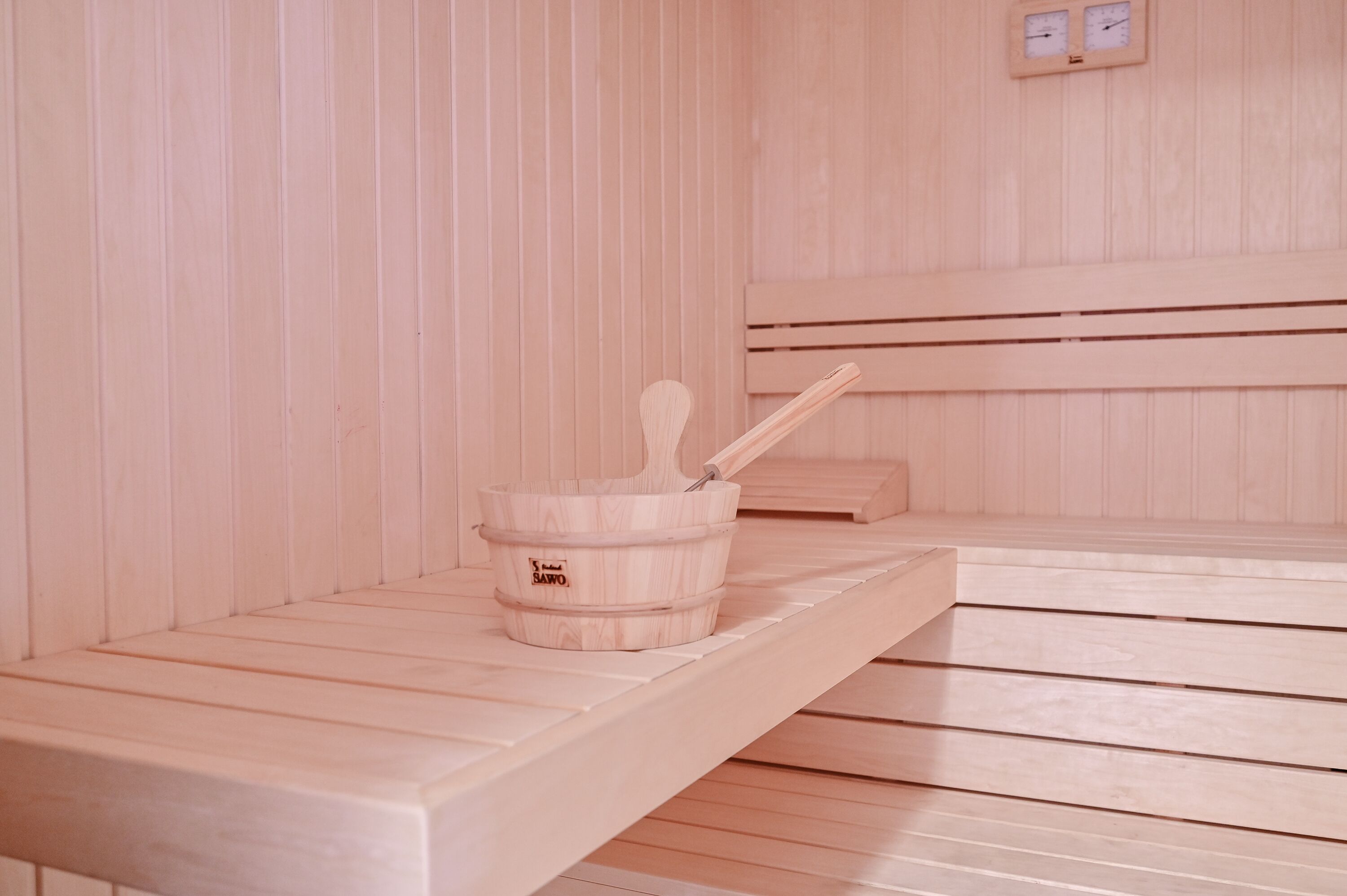 Un sauna avec des bancs en bois et un seau en bois accompagné d’une louche.