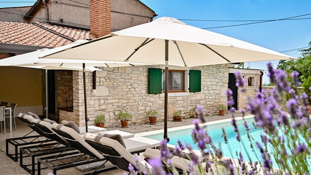 A poolside area with lounge chairs, a large umbrella, and potted plants.
