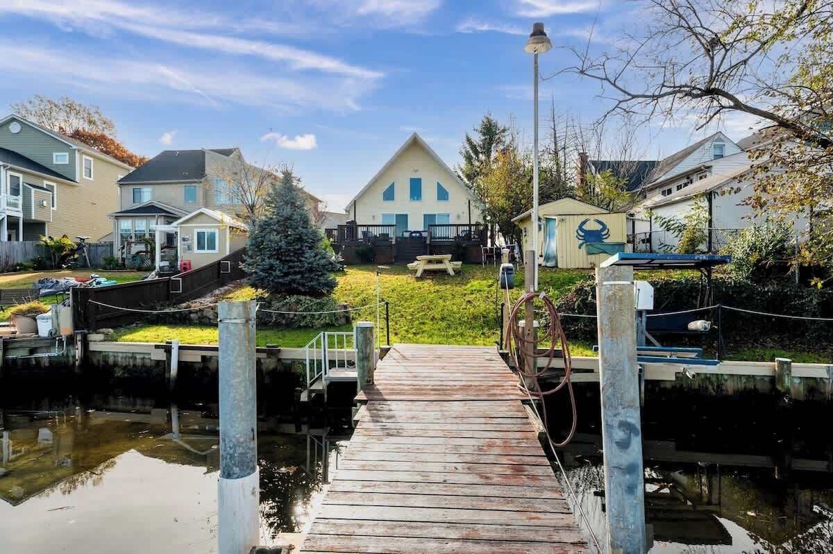 A wooden dock leading to a house with a large front yard and a Christmas tree.