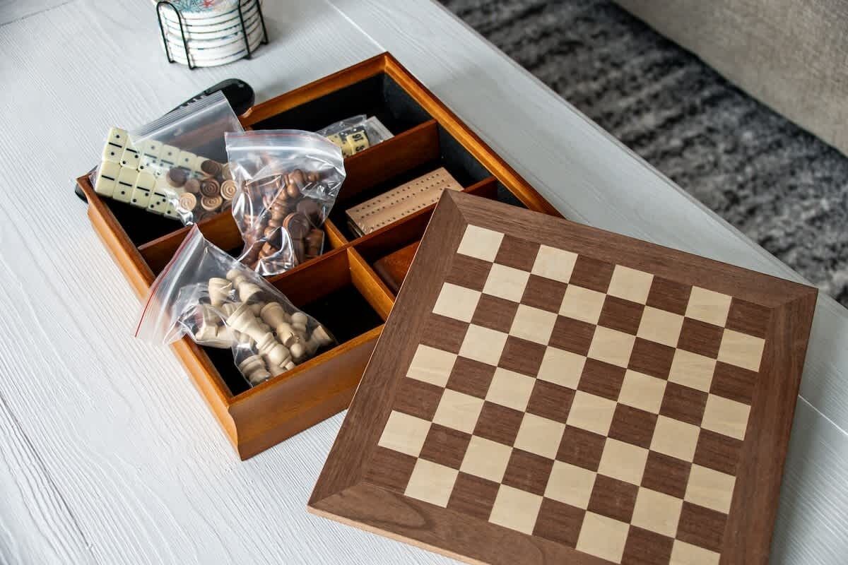 A wooden chessboard with a checkered pattern, placed on a white surface with a drawer containing various items including a bag of nuts and a small box.