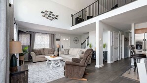 Amplia sala de estar con sofá, sillón y mesa de centro. Una escalera conduce a un nivel superior.