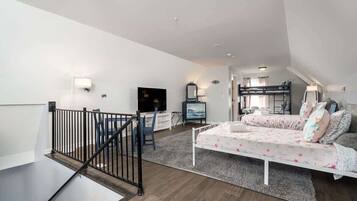 A modern apartment with a loft-style bedroom, a living area with a sofa and TV, and a staircase with a railing.