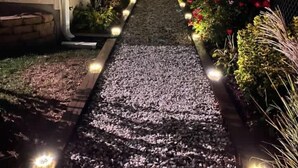 Un camino que lleva a una casa, con suelo de grava y parterres a ambos lados.