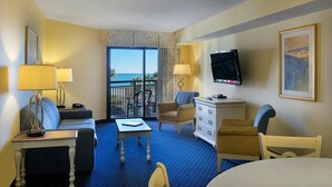 A hotel room with a balcony, a sofa, a chair, a table, a TV, and a dresser. - Coastal Bliss  Ocean View 2BR Condo on 4th Floor (Myrtle Beach)