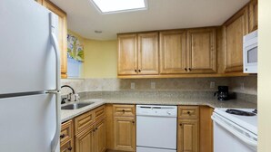 A kitchen with wooden cabinets, a dishwasher, a refrigerator, a microwave, and a coffee maker. - Coastal Bliss  Ocean View 2BR Condo on 4th Floor (Myrtle Beach)