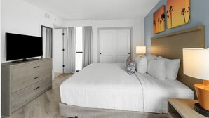 A hotel room with a large bed, a TV, a desk with a lamp, and artwork on the wall.