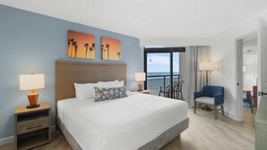 A hotel room with a large bed, two nightstands, a chair, and a view of the ocean.