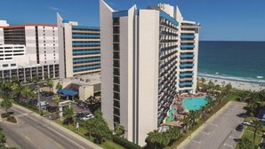 A hotel with multiple high-rise buildings, a swimming pool, and a beach view.