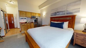 Un dormitorio con cama de madera, una mesita de noche y vistas al área de la cocina.