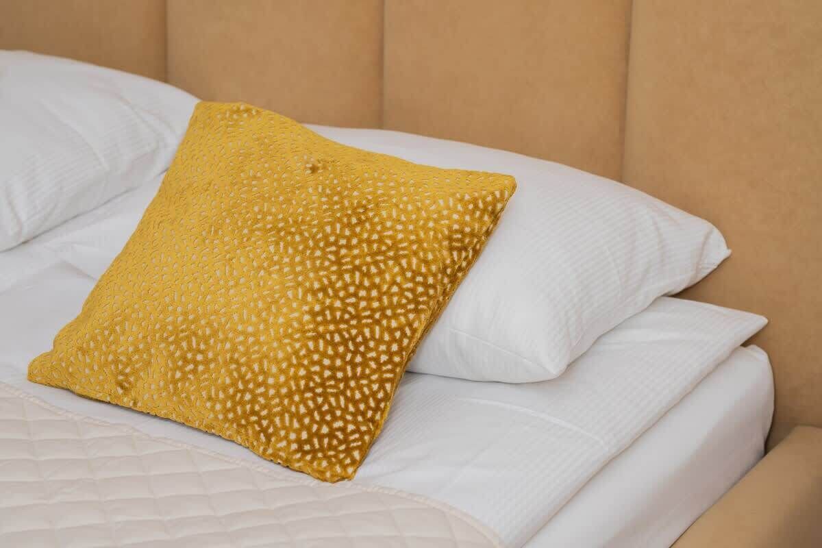 Een bed met witte lakens en één mosterdgeel kussen.