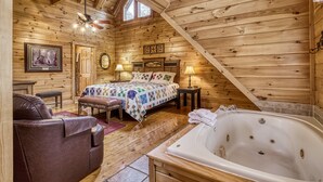 A log cabin bedroom with a large bed, a sitting area with a leather couch, a wooden ceiling, and a bathtub. - Spacious 4BR Cabin w/ Game Room, Hot Tub & Pools – 3 Miles to Parkway (Sevierville)