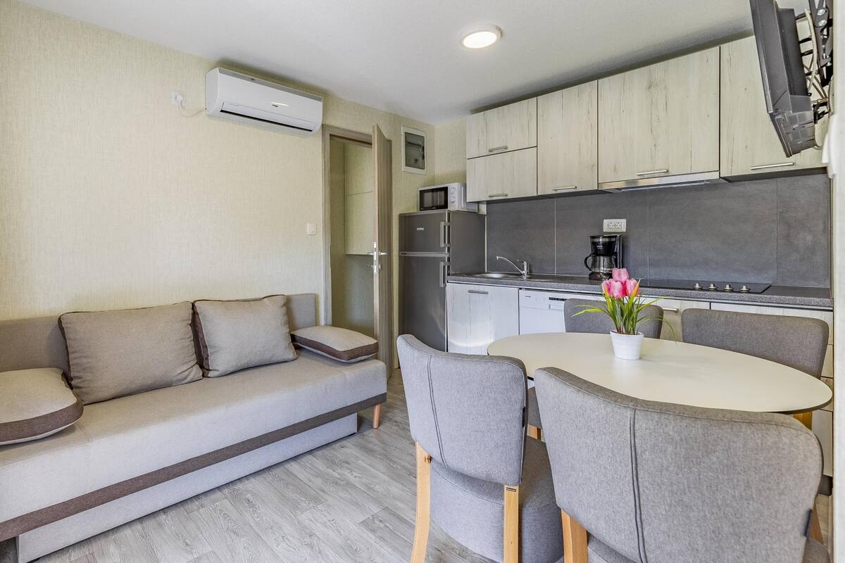 Uma kitchenette compacta equipada com frigorífico, micro-ondas, máquina de café e uma pequena mesa de jantar com cadeiras.