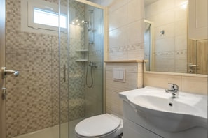A bathroom with a glass-enclosed shower, a white toilet, and a sink with a mirror above it. - Mobile Homes with Shared Pool Rocco 2 (Medulin)