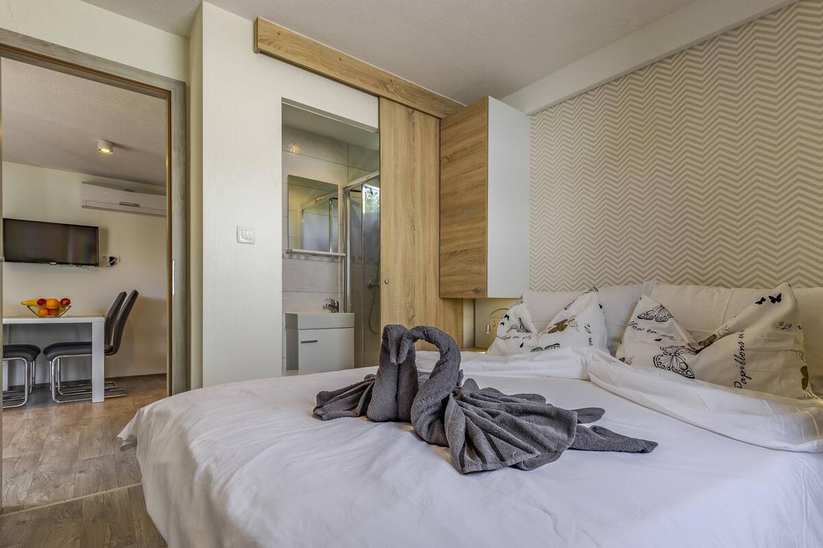 Quarto de hotel com cama, escrivaninha com cadeira, televisão e banheiro com espelho e chuveiro.