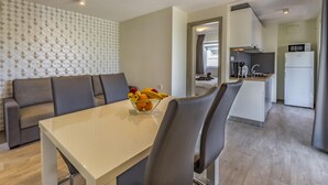 A modern living room with a sofa, a dining table with fruit, and a kitchen area with a refrigerator and coffee maker. - Mobile Homes with Shared Pool Rocco 2 (Medulin)