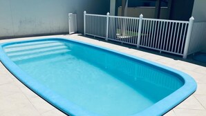 Ein rechteckiger Swimmingpool mit weißem Zaun und Fliesenboden.