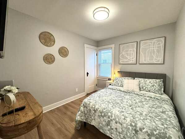 Un dormitorio con cama, mesita de noche con lámpara, una puerta y tres adornos en la pared.