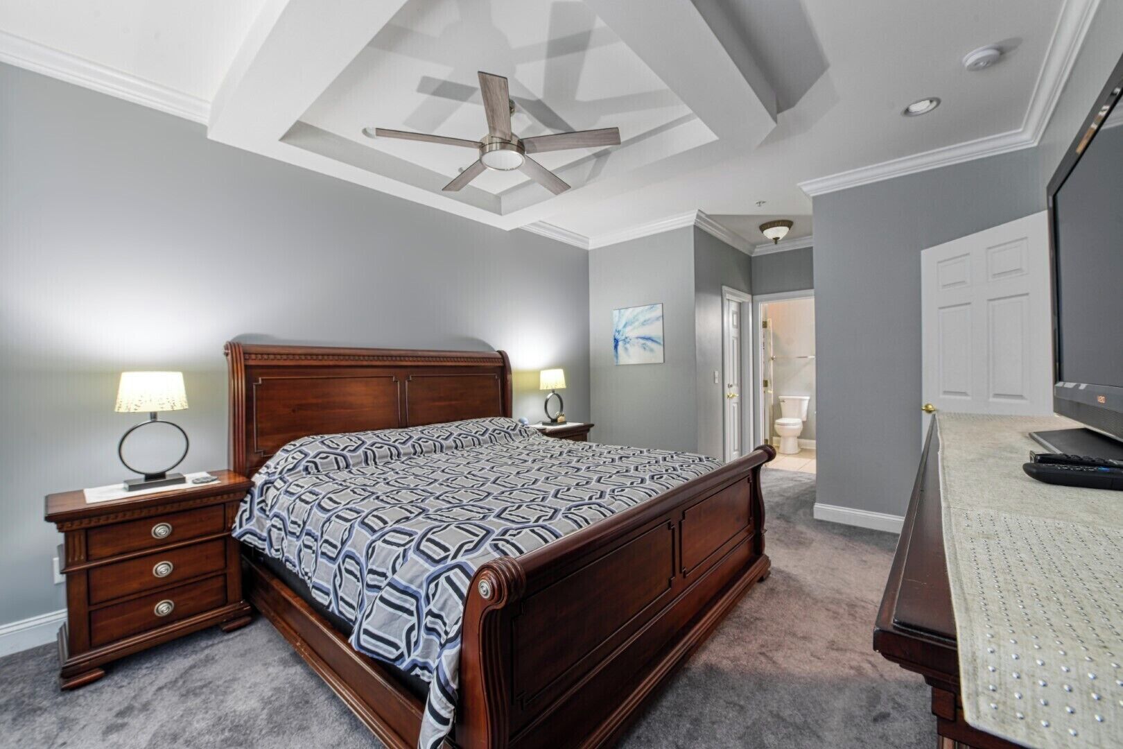 A bedroom with a wooden bed, nightstands with lamps, a ceiling fan, and a TV on a stand.