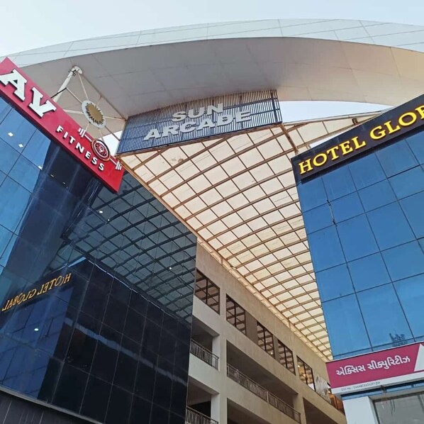 A modern building with a large glass facade, a fitness center sign, and a hotel sign. - Hotel Global (Surat)