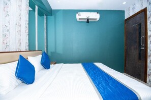 A hotel room with a bed, blue pillows, a white air conditioner, and a teal wall. - Hotel Global (Surat)